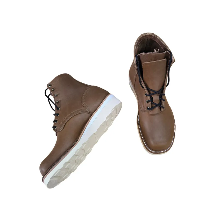 A pair of brown six-inch lace-up work boots with white wedge soles on a white background, one standing in profile and one seen from above.