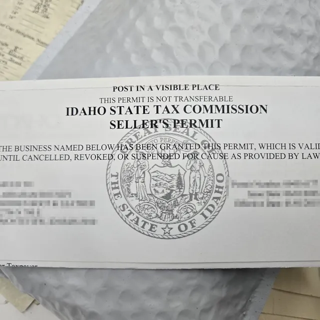 An Idaho State Tax Commission seller's permit lying on a workbench, headed 'Post in a visible place'. The holder's details and the permit number are pixelated.