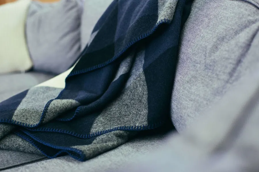 A navy, grey, and cream buffalo-check wool throw blanket draped over a grey sofa with matching throw pillows.