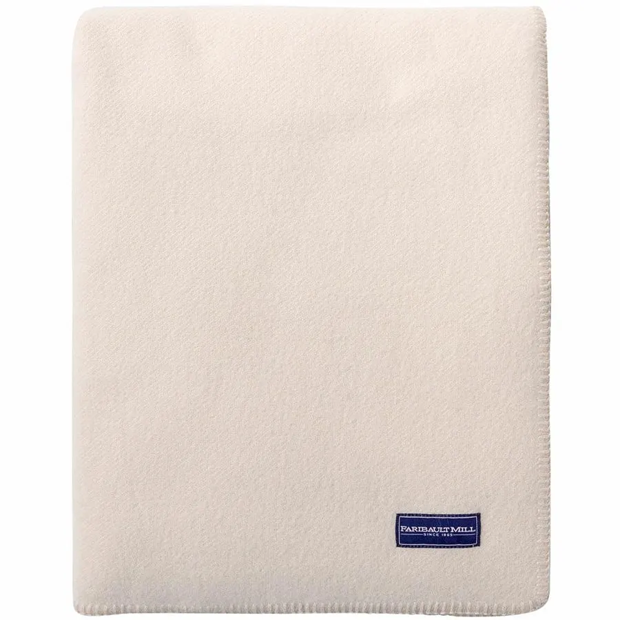 A folded bone-white wool blanket with a whipstitched edge and a navy Faribault Mill label, standing upright against a white background.