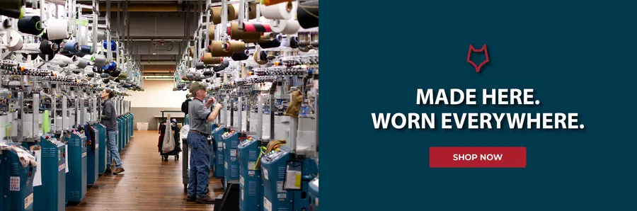 Two workers tend knitting machines in the Fox River factory beside a navy panel reading “Made here. Worn everywhere.”
