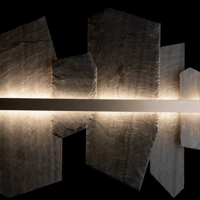 Close angled detail of a linear LED pendant's slate-shard panels lit from behind along a slim bronze bar, against a black background.