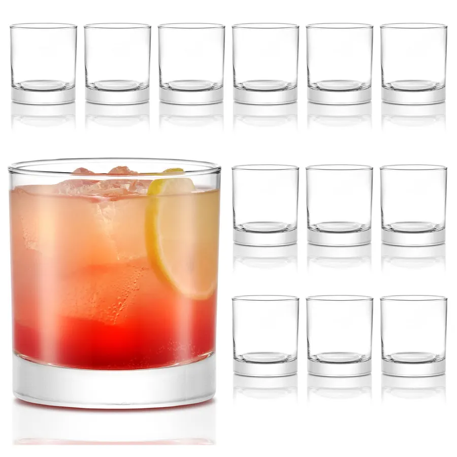 A dozen clear heavy-base rocks glasses arranged in rows, with one filled with a red cocktail, ice and a lemon slice in front, against a white background.