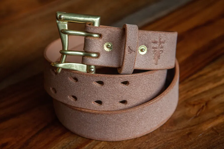 A coiled tan roughout suede leather belt with a brass double-prong buckle and diamond-shaped perforations, on a wood-plank surface.