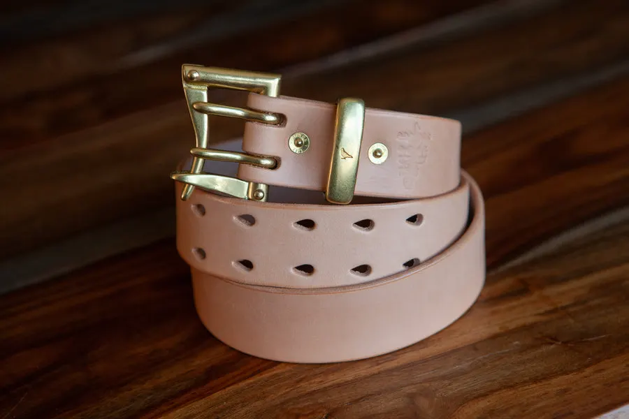 A coiled smooth natural vegetable-tanned leather belt with a brass buckle and diamond-shaped perforations, on a wood-plank surface.