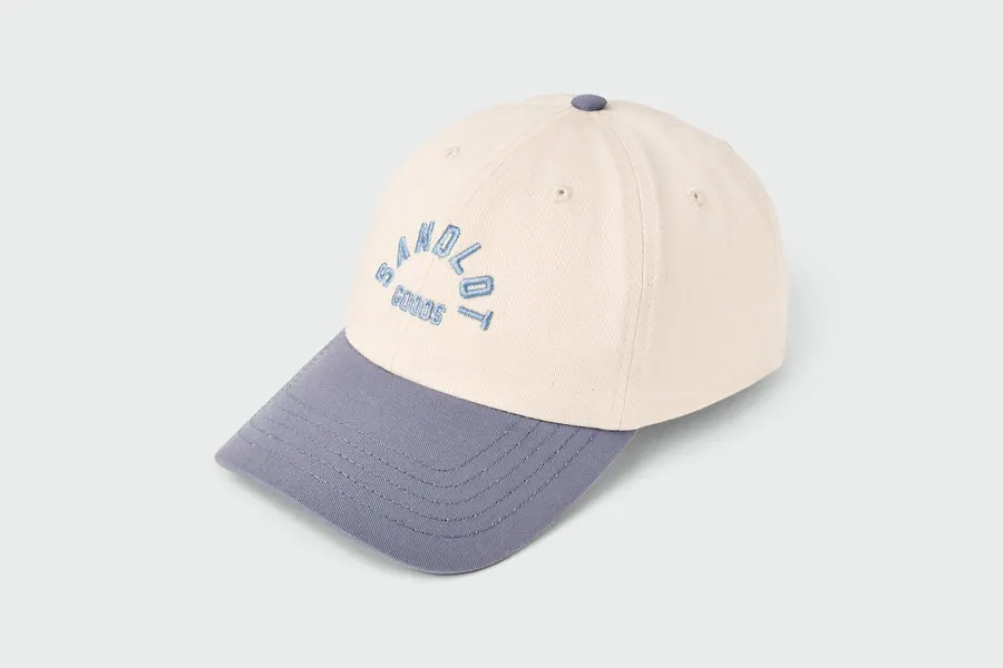 A cream and slate-blue six-panel dad hat with an embroidered blue 'Sandlot Goods' arch logo on the front panel.