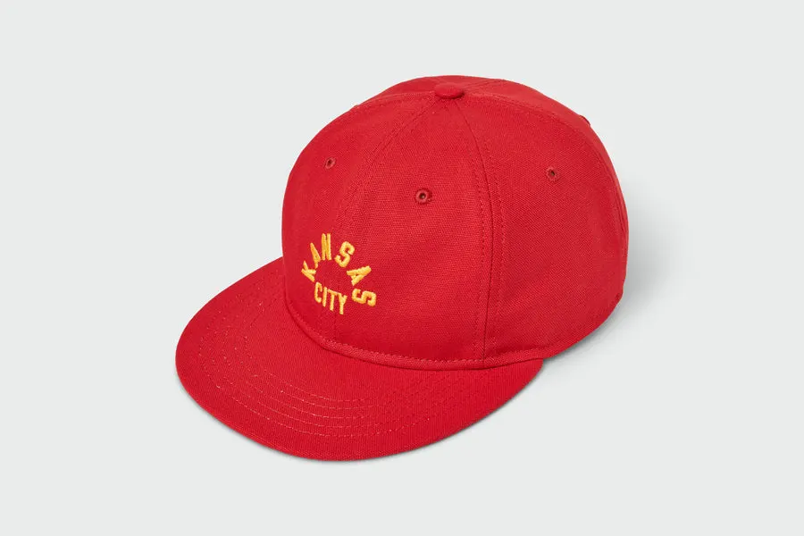 A red flat-brim cap with a yellow embroidered arched 'Kansas City' wordmark on the front panel.