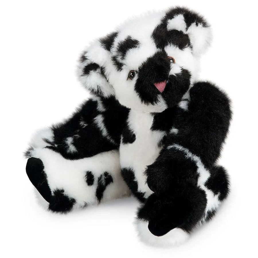 A black-and-white spotted plush teddy bear sitting with legs splayed against a plain white background.