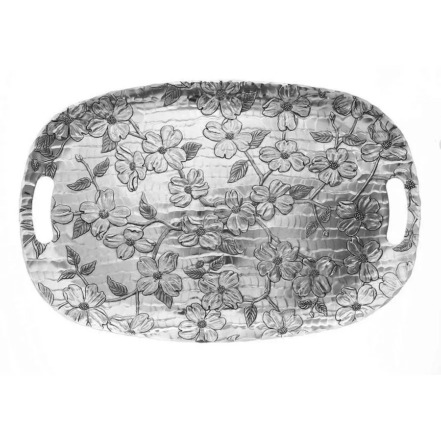 An oval hand-hammered aluminum tray with two cutout handles, embossed all over with a dogwood blossom and branch pattern, on a white background.